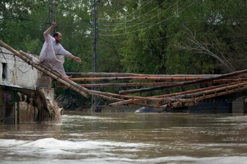 A man tries to cross a makeshift bridge to escape his flooded home
